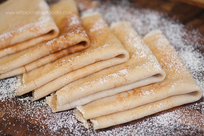 a stack of folded crepes with powdered sugar