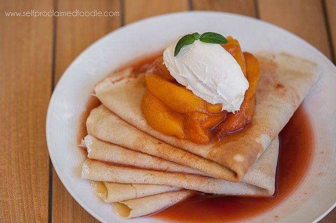 a stack of homemade crepes topped with cooked peaches and whipped cream