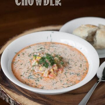 A bowl of salmon chowder in white bowl with a split roll on the side