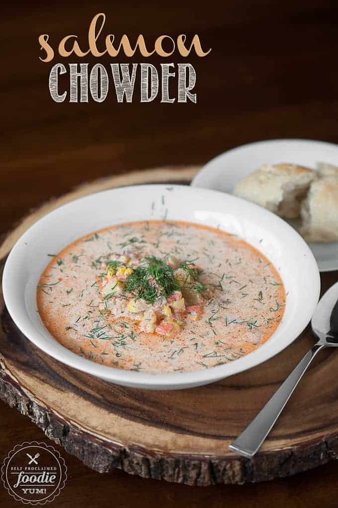 A bowl of salmon chowder in white bowl with a split roll on the side