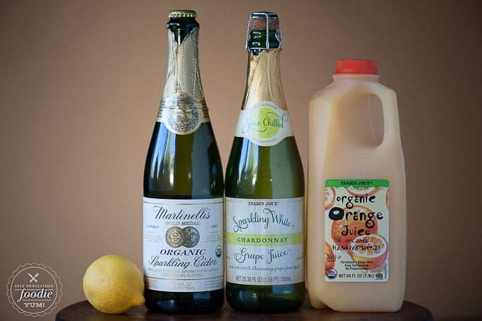 a lemon and bottles of sparkling apple cider, sparkling grape juice, and orange juice