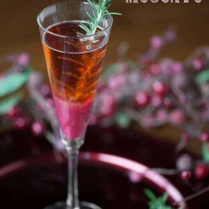 champagne flute with a cranberry pear moscato cocktail with rosemary garnish