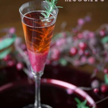 champagne flute with a cranberry pear moscato cocktail with rosemary garnish