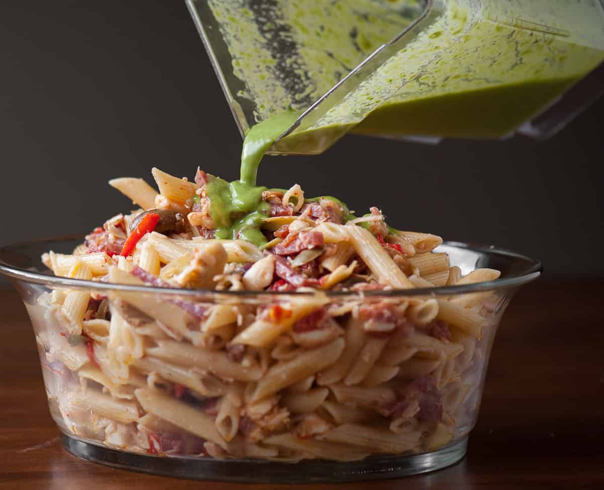 pouring homemade dressing onto antipasto pasta salad.