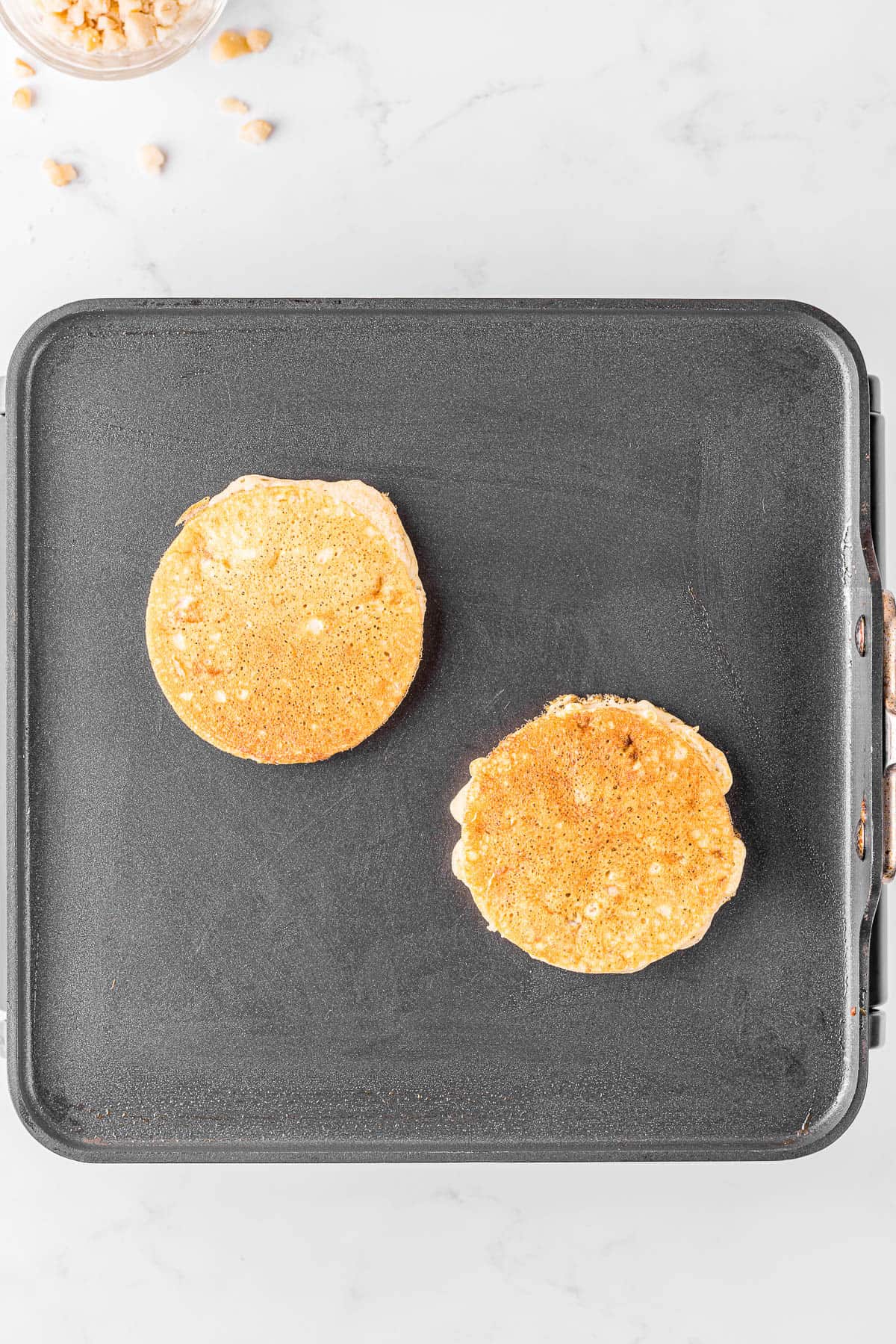two Fluffy banana pancakes cooking on hot griddle.