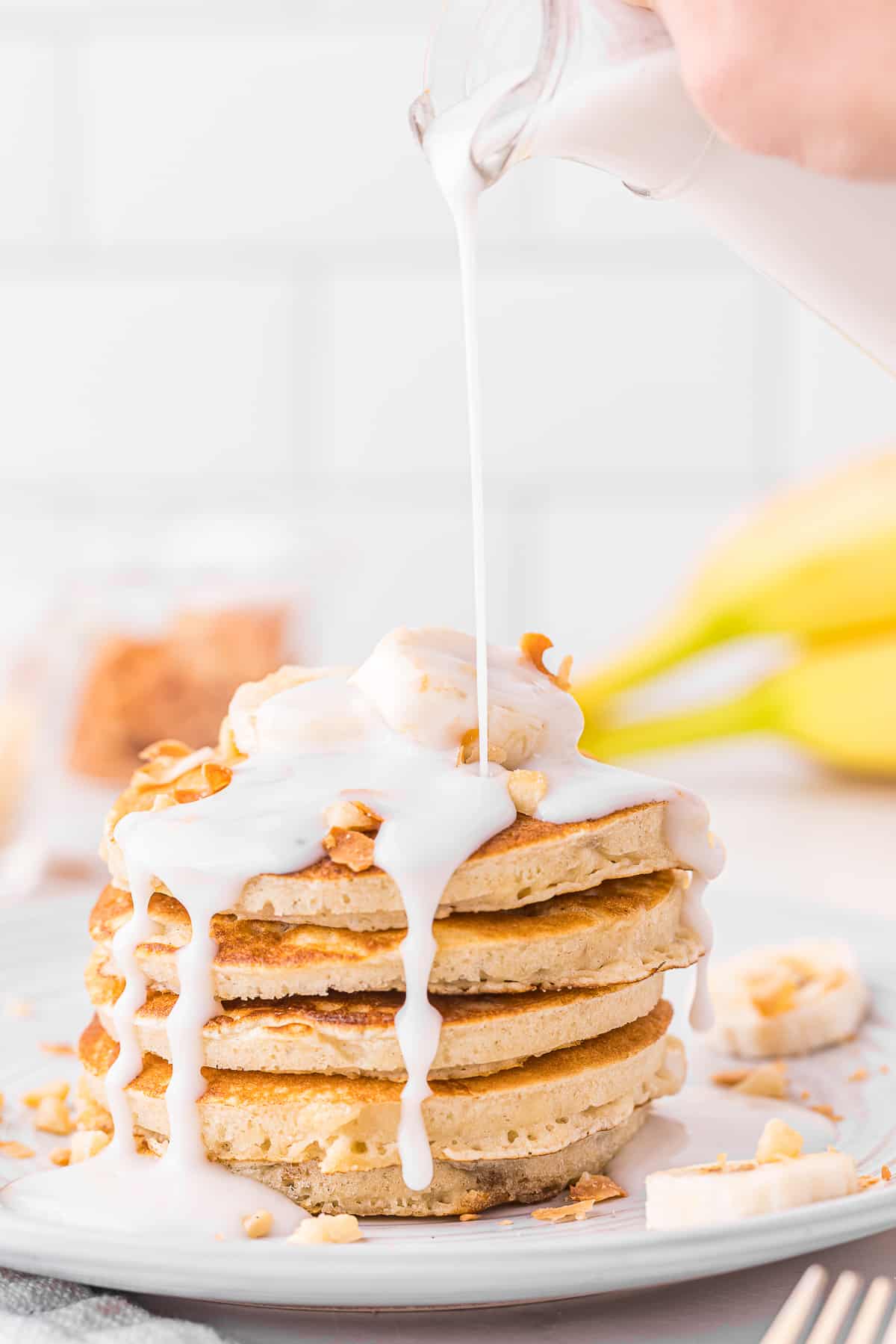 drizzling coconut syrup on top of Maui-inspired banana mac pancakes