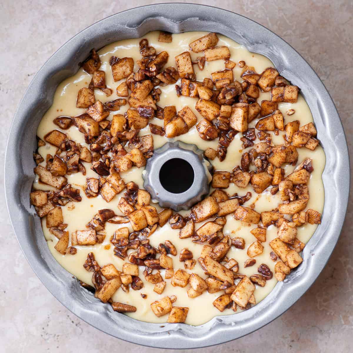 adding cinnamon sugar apples to cake batter in a bundt pan.
