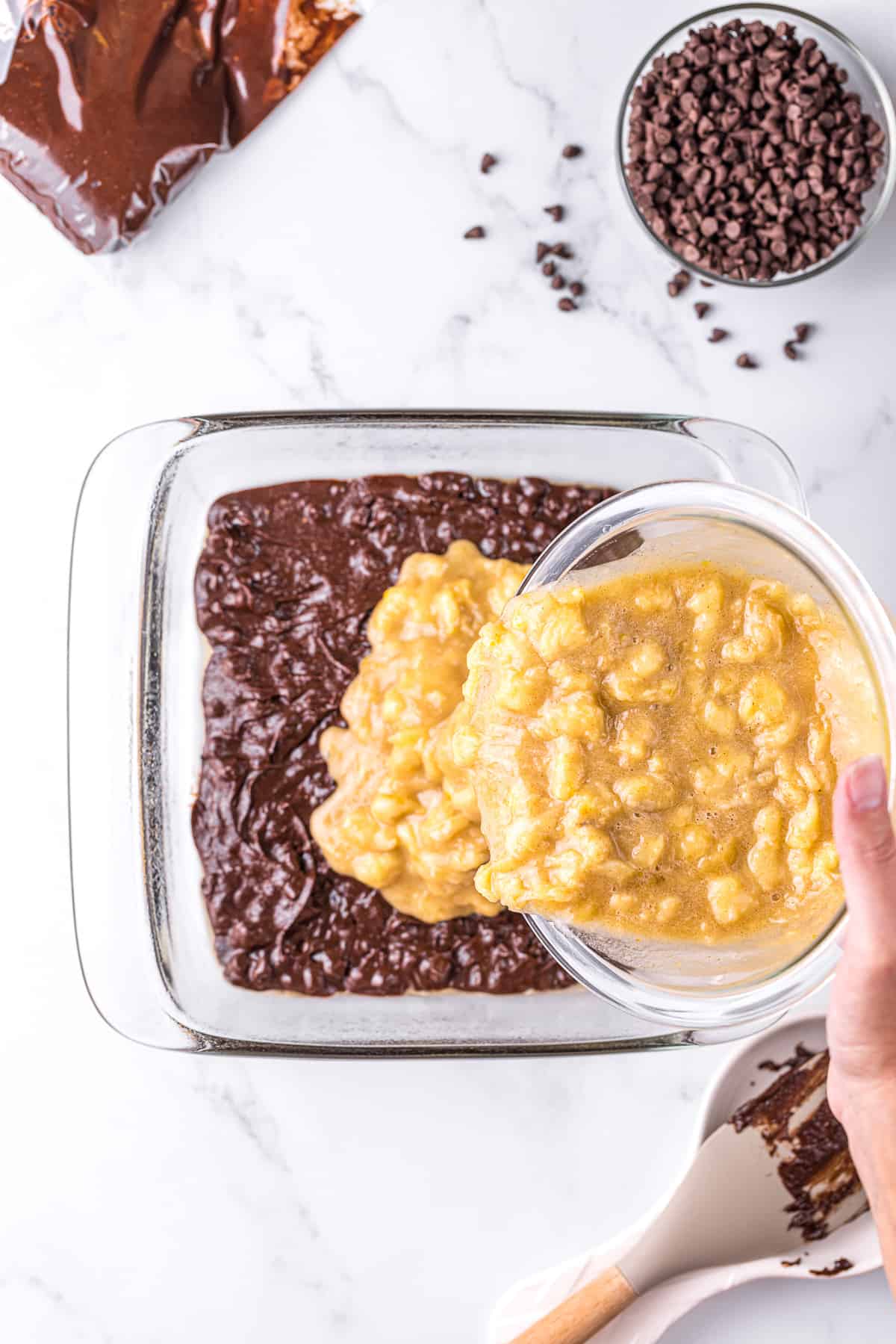 adding mashed banana batter on top of brownie batter in baking dish.