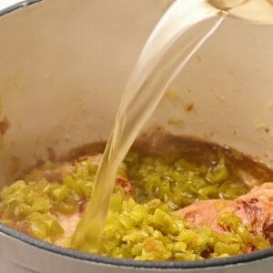 adding chicken broth and green chile to chicken breasts.