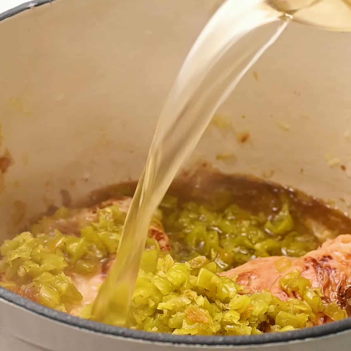 adding chicken broth and green chile to chicken breasts.
