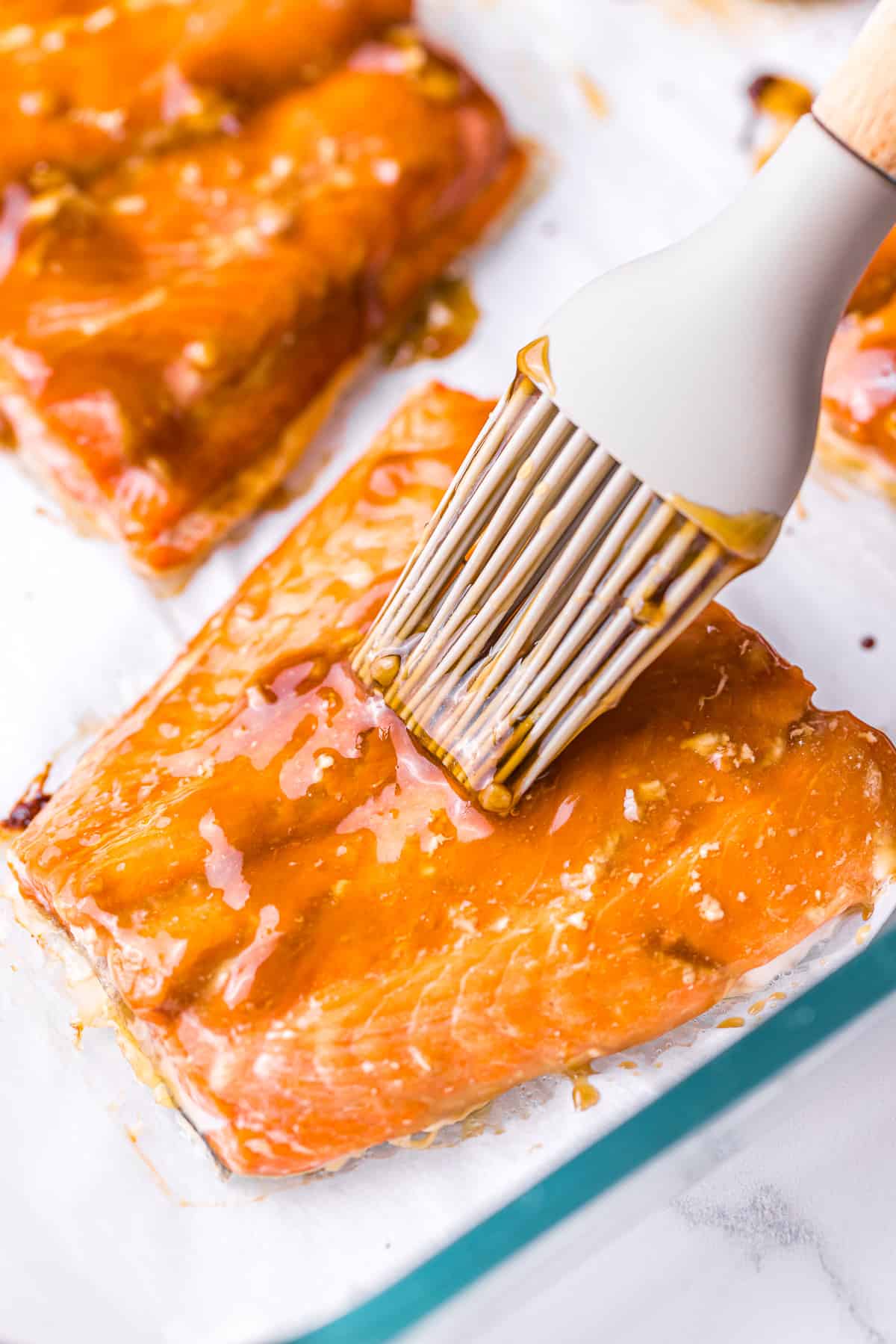 A baking dish filled with glistening salmon fillets coated in thick teriyaki sauce.