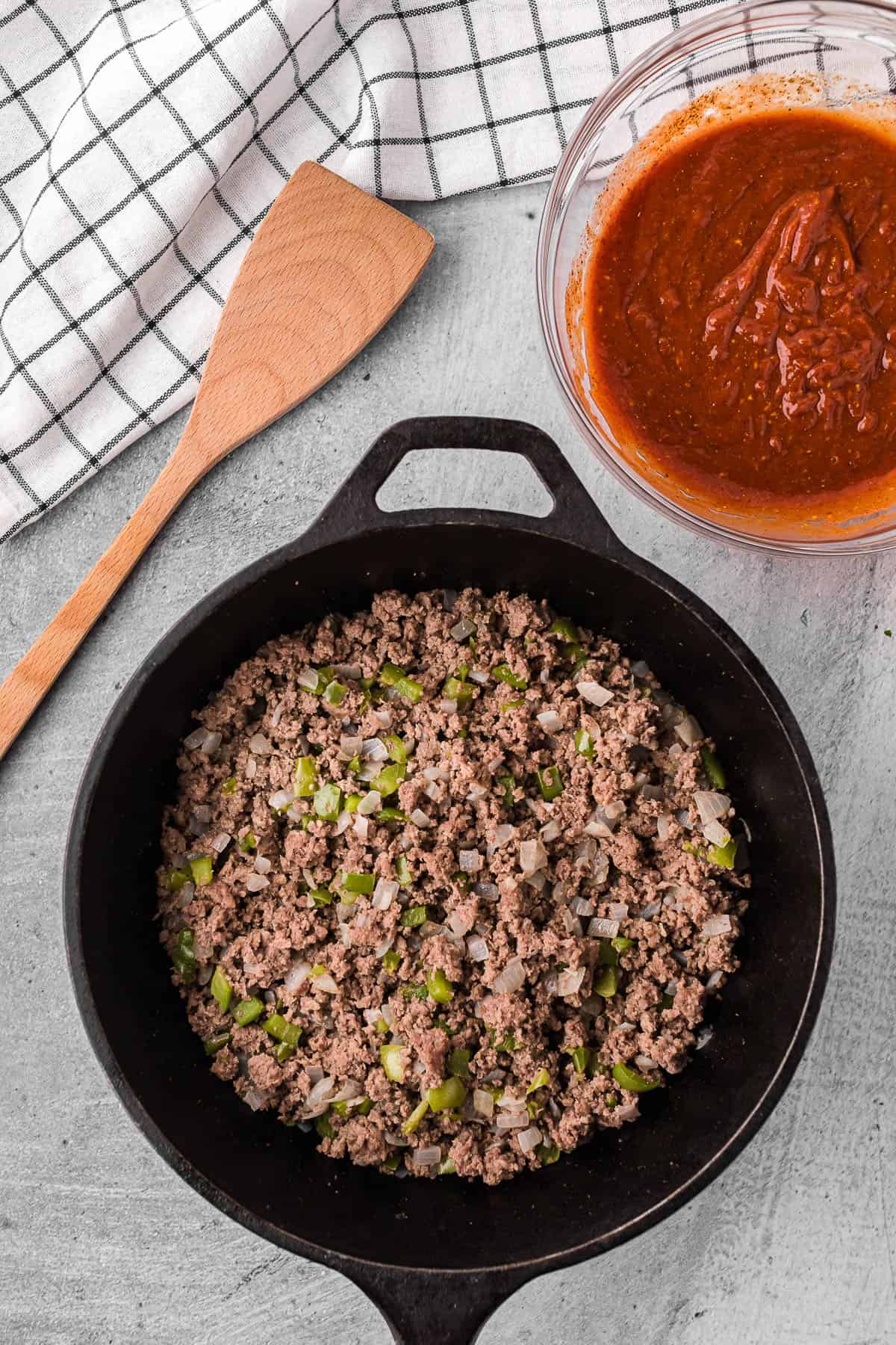 Ground beef with diced onion and green peppers in cast iron skillet.