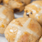 Recipe for homemade hot cross buns with raisins, dried apricots, and an orange glaze.