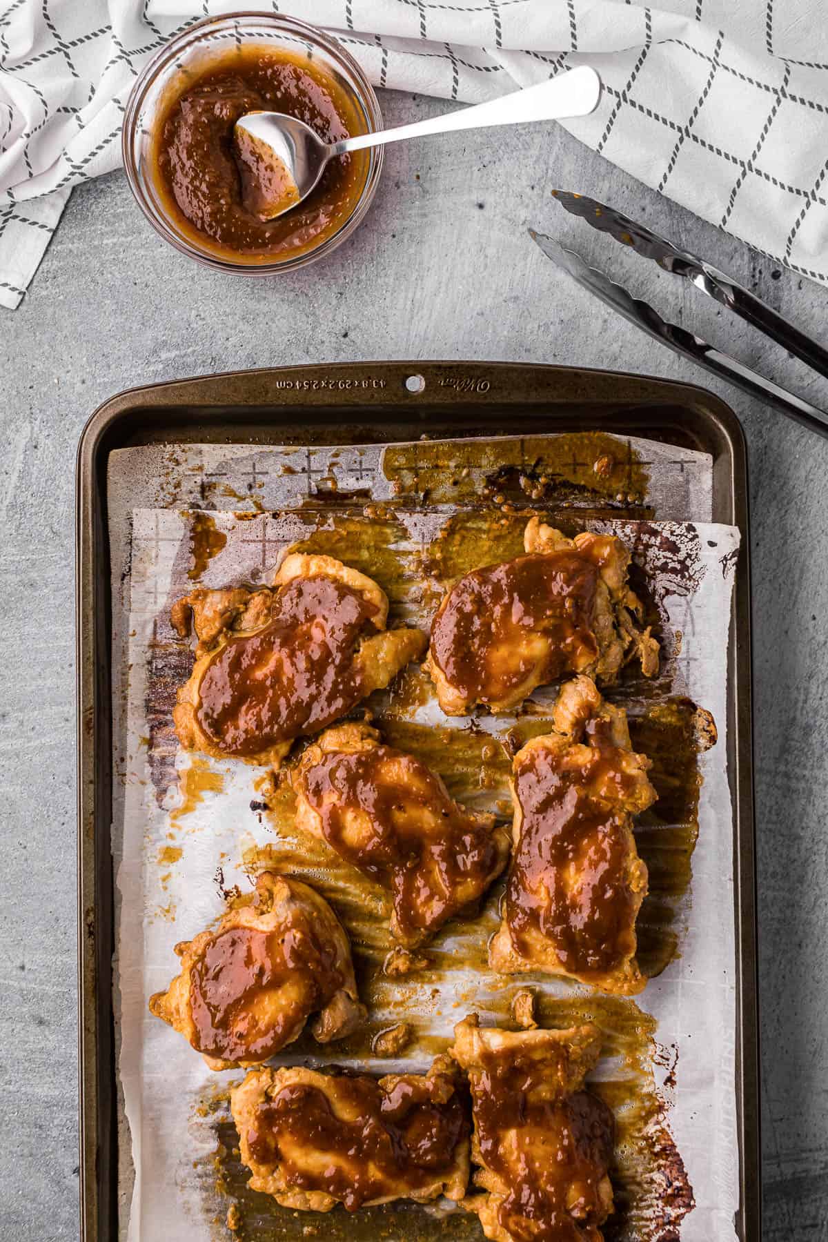 apricot glazed chicken thighs on baking sheet with small bowl of glaze.