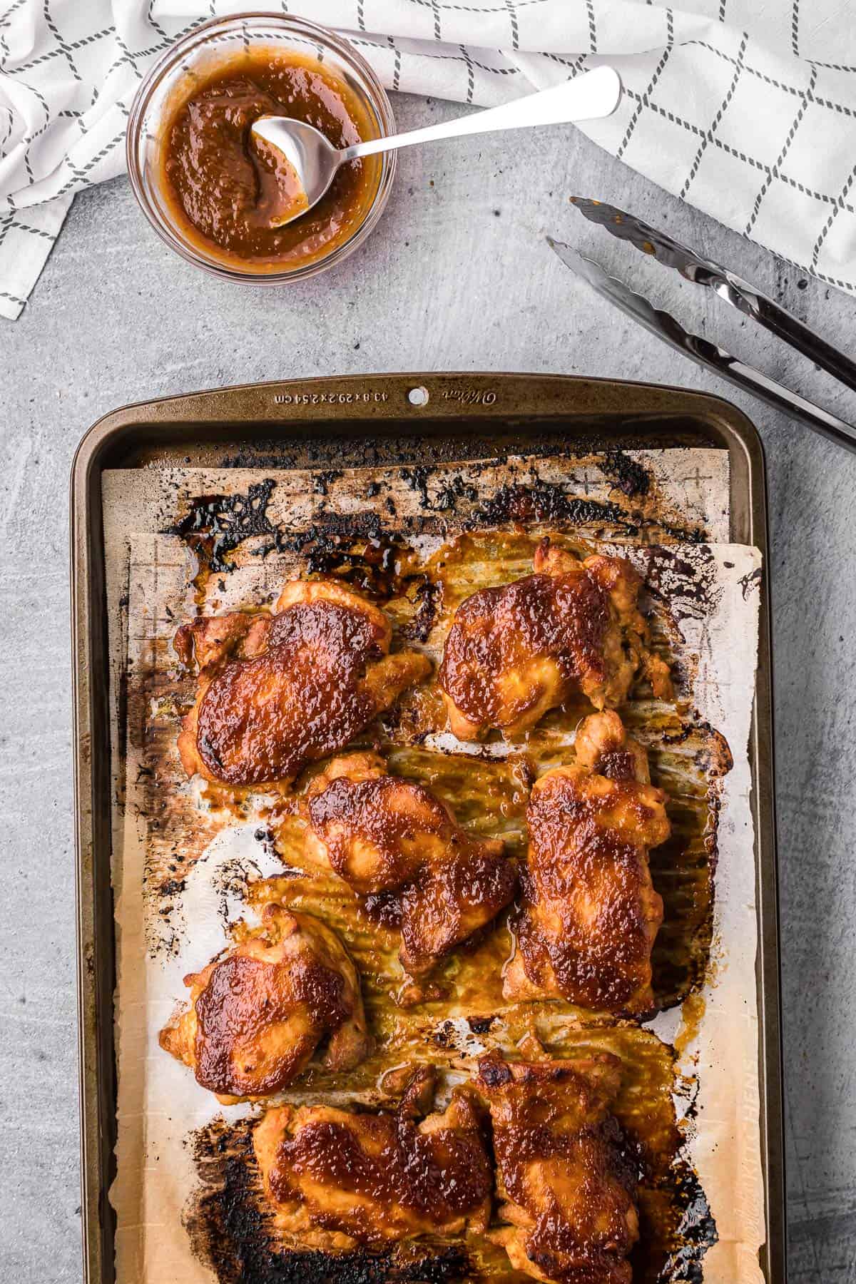 apricot glazed chicken thighs on baking sheet with small bowl of glaze.