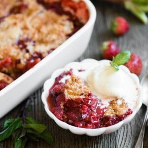 strawberry rhubarb cobbler in small white dish with ice cream on top