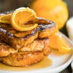 stack of brioche French toast with orange slices and syrup.