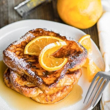 stack of brioche French toast with orange slices and syrup.