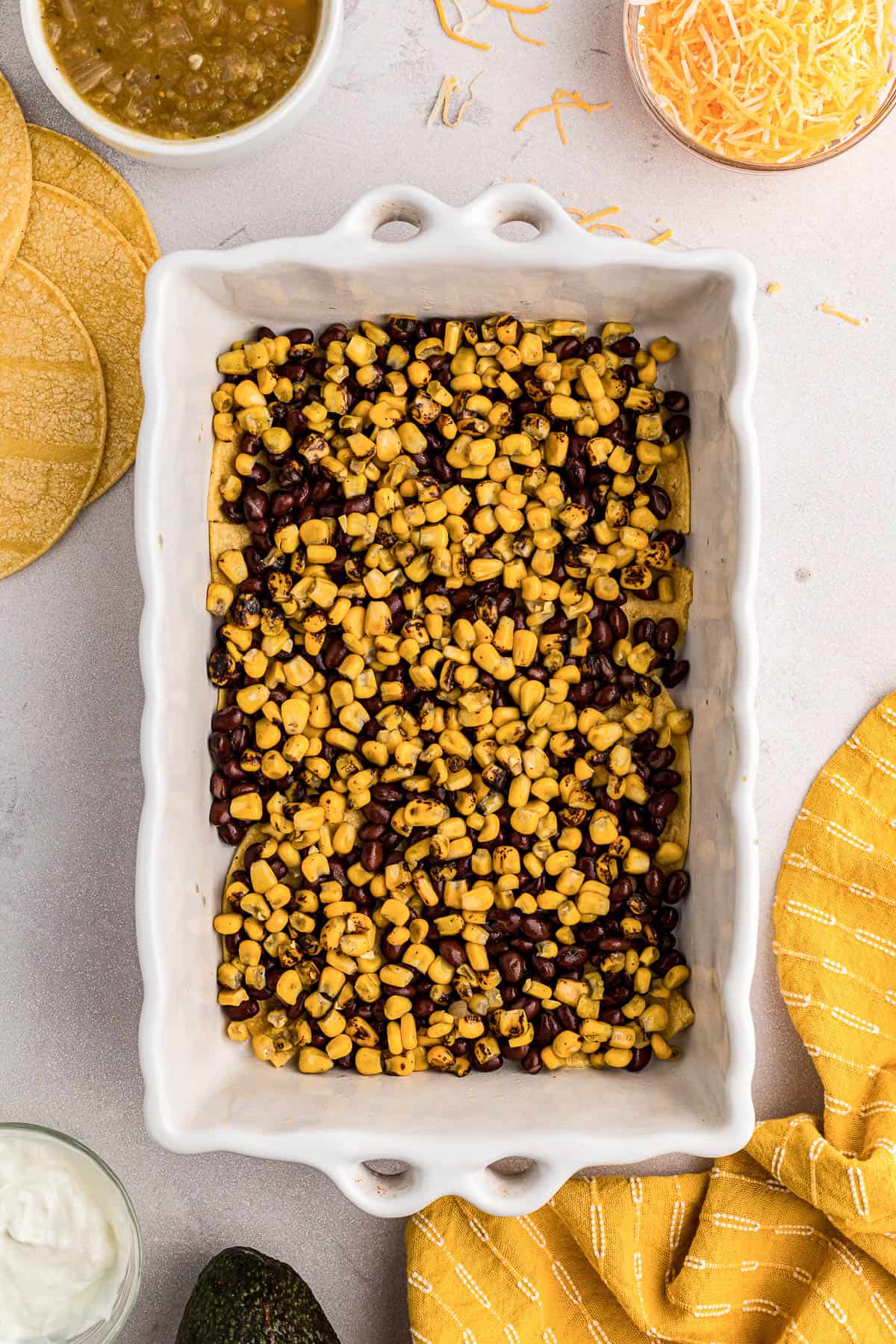 black beans and corn on top of corn tortilla slices in a white casserole dish.