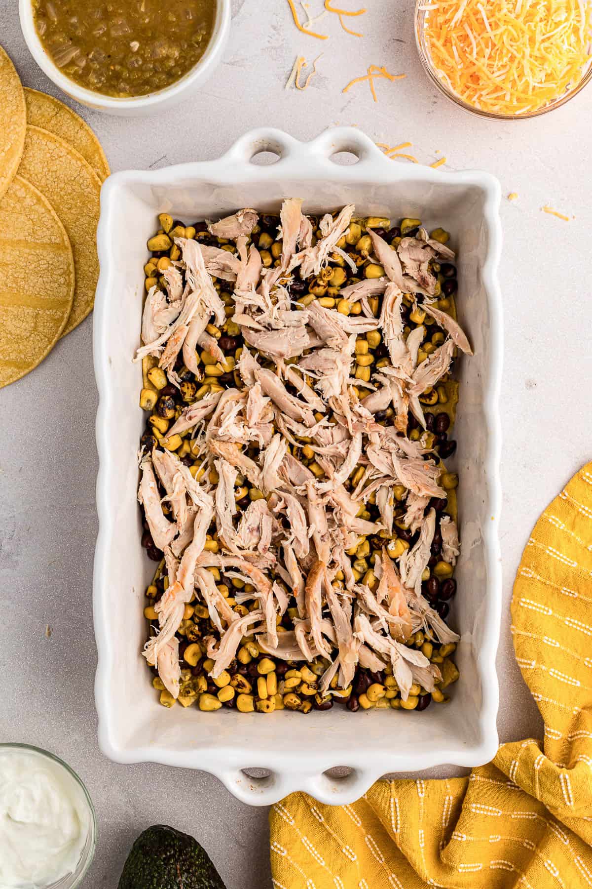 Shredded chicken on top of black beans and corn in a casserole dish for a chicken enchilada recipe.