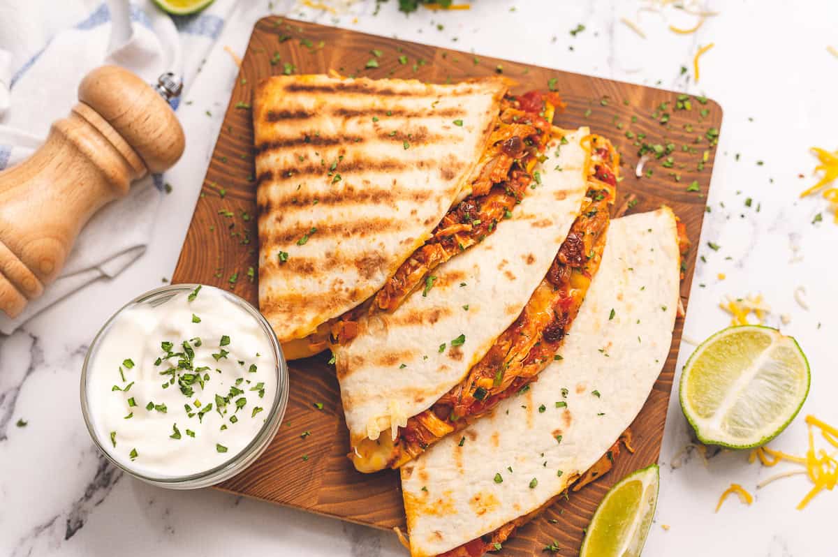 three quesadilla slices filled with shredded chipotle chicken with a side of sour cream.