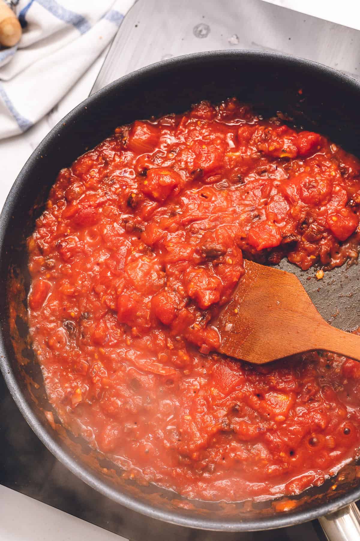 cooking canned tomatoes and chipotle peppers in a sauté pan with a wooden spoon.