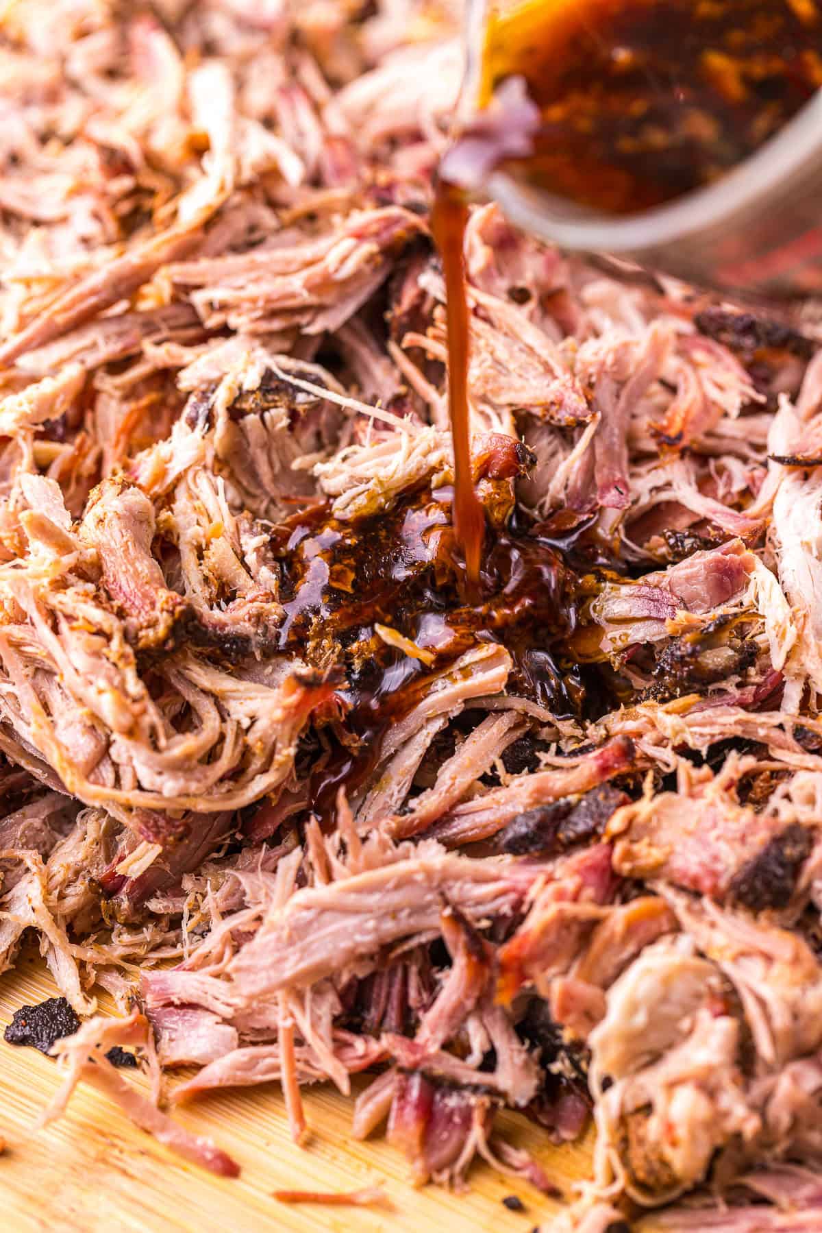 Pouring cooking liquid over shredded pulled pork shoulder.