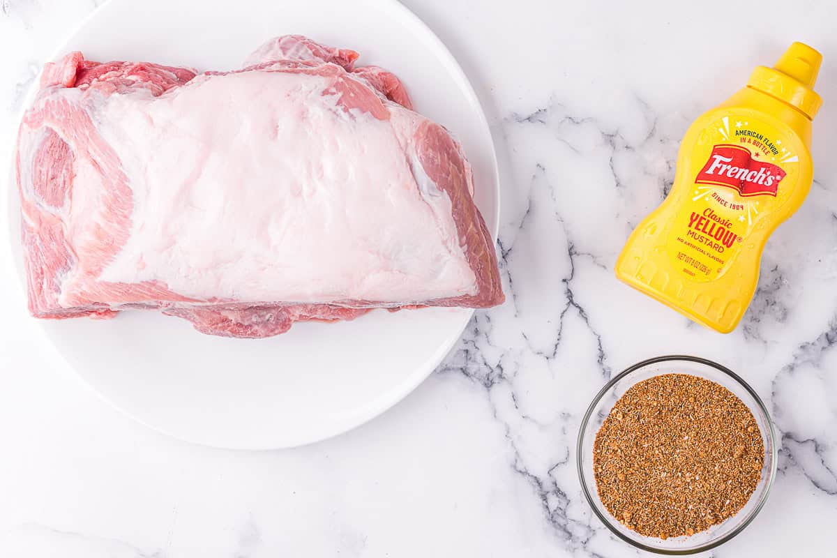 uncooked pork shoulder roast, mustard, and dry rub seasonings.