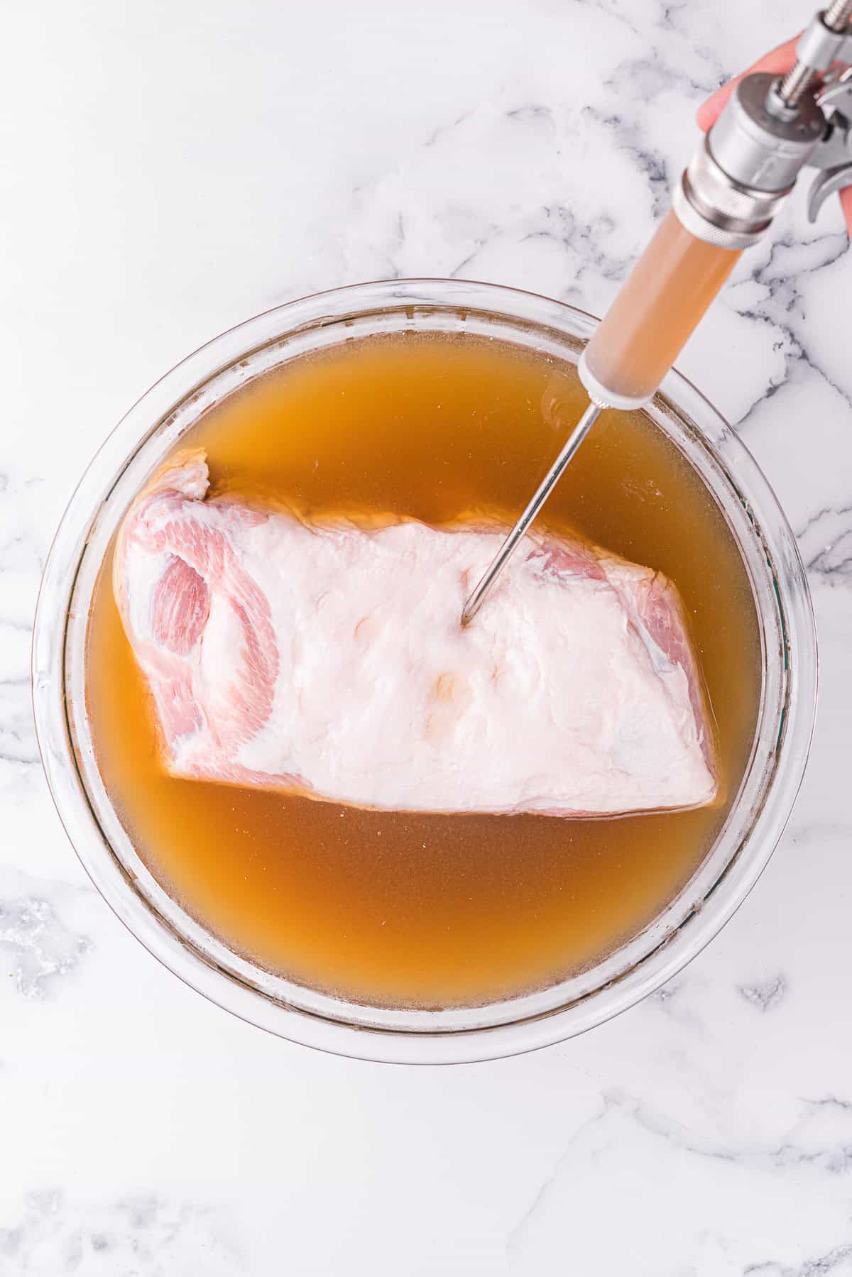 injecting a pork shoulder roast with apple cider brine prior to smoking it on the grill.