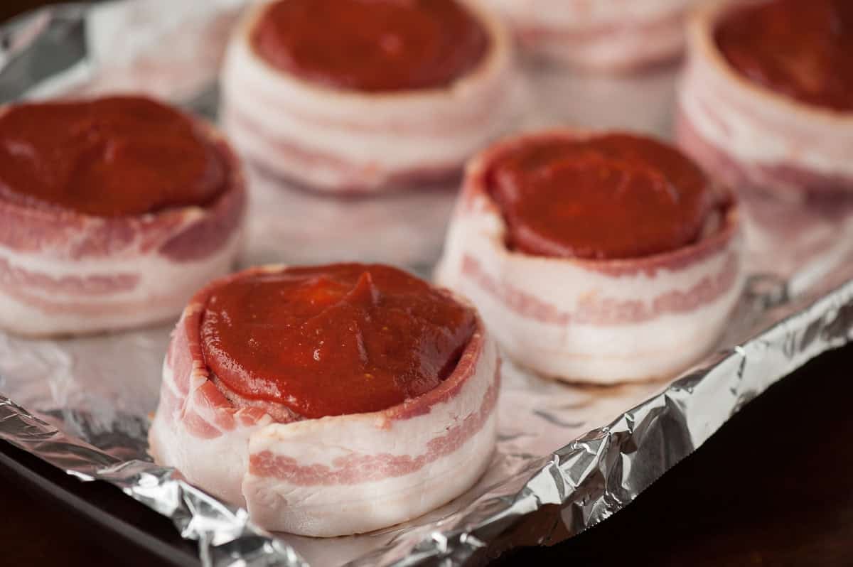 making individual bacon wrapped meatloaf with ketchup topping.