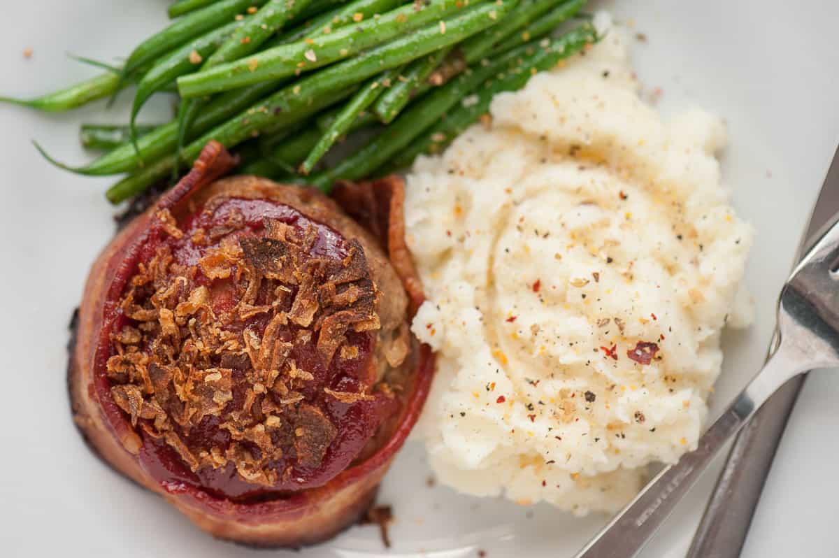 bacon wrapped meatloaf with mashed potatoes and green beans.