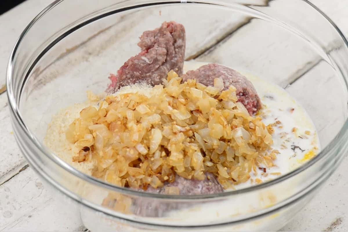 mixing sauteed onions with ground beef and other ingredients to make meatloaf.