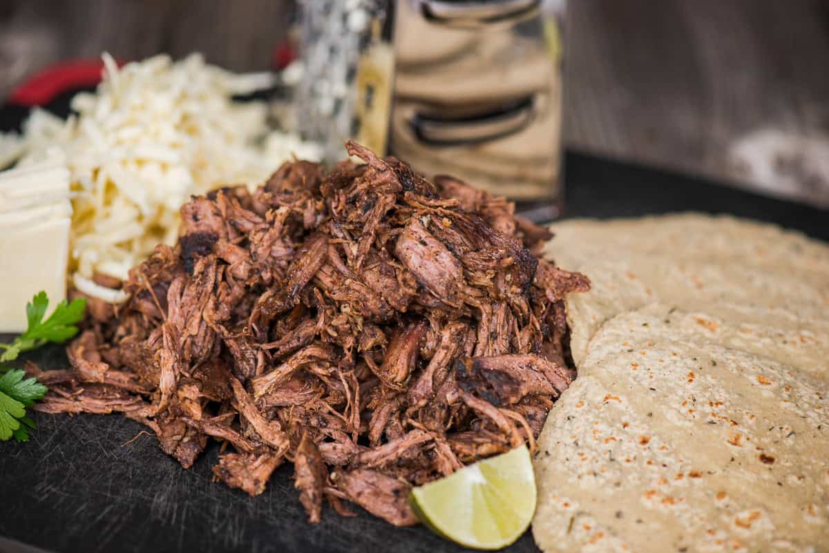 Shredded beef barbacoa with corn tortillas and shredded cheese.