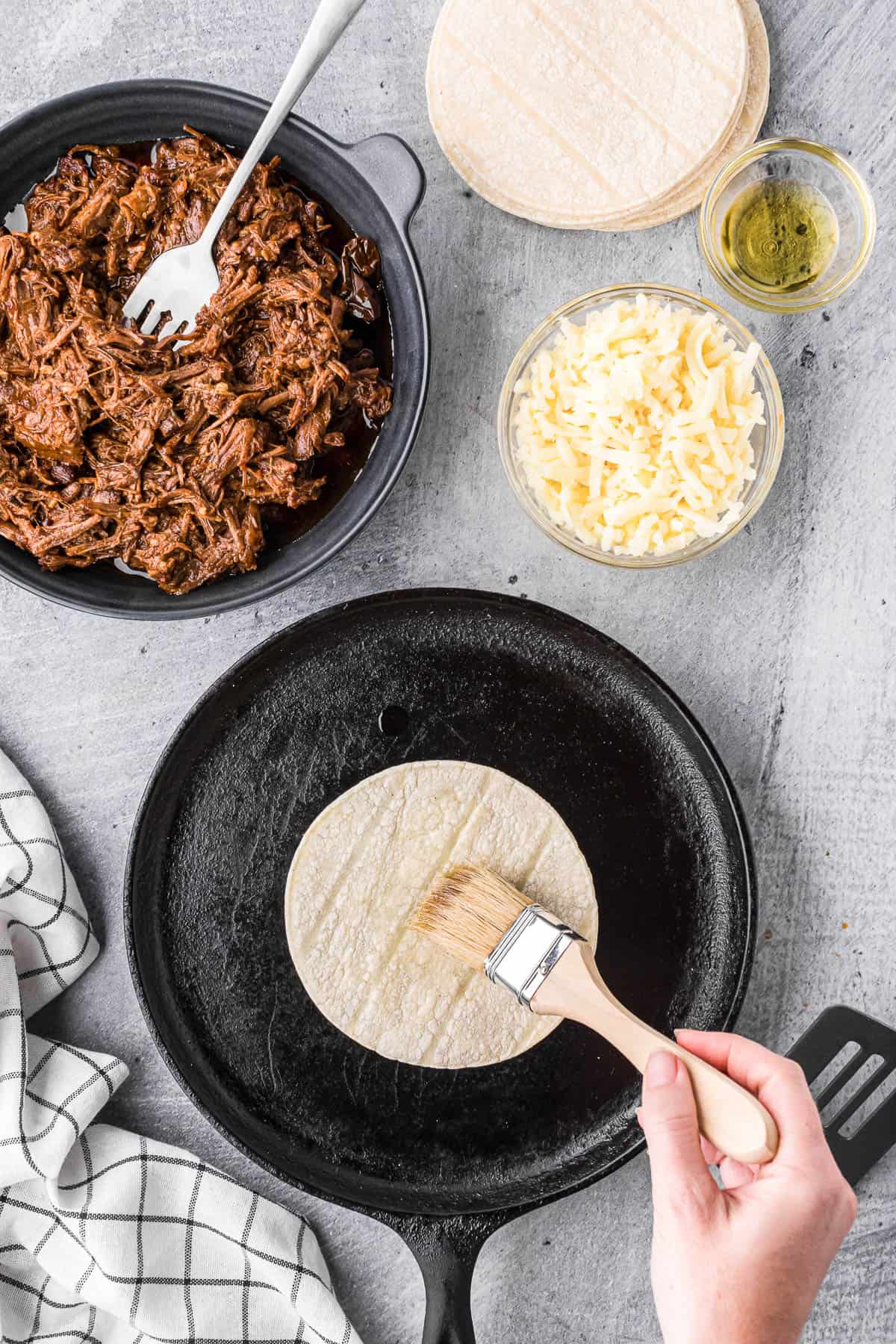 adding a thin layer of oil to a corn tortilla to make a barbacoa quesadilla.