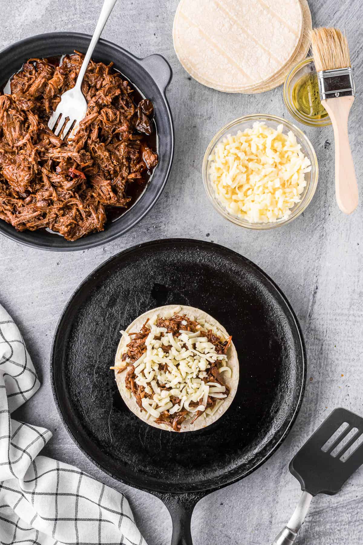 layering shredded cheese and shredded beef barbacoa for quesadillas.