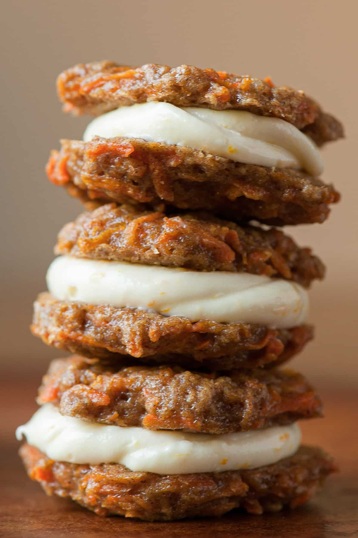 stack of three carrot cake sandwich cookies with cream cheese frosting.