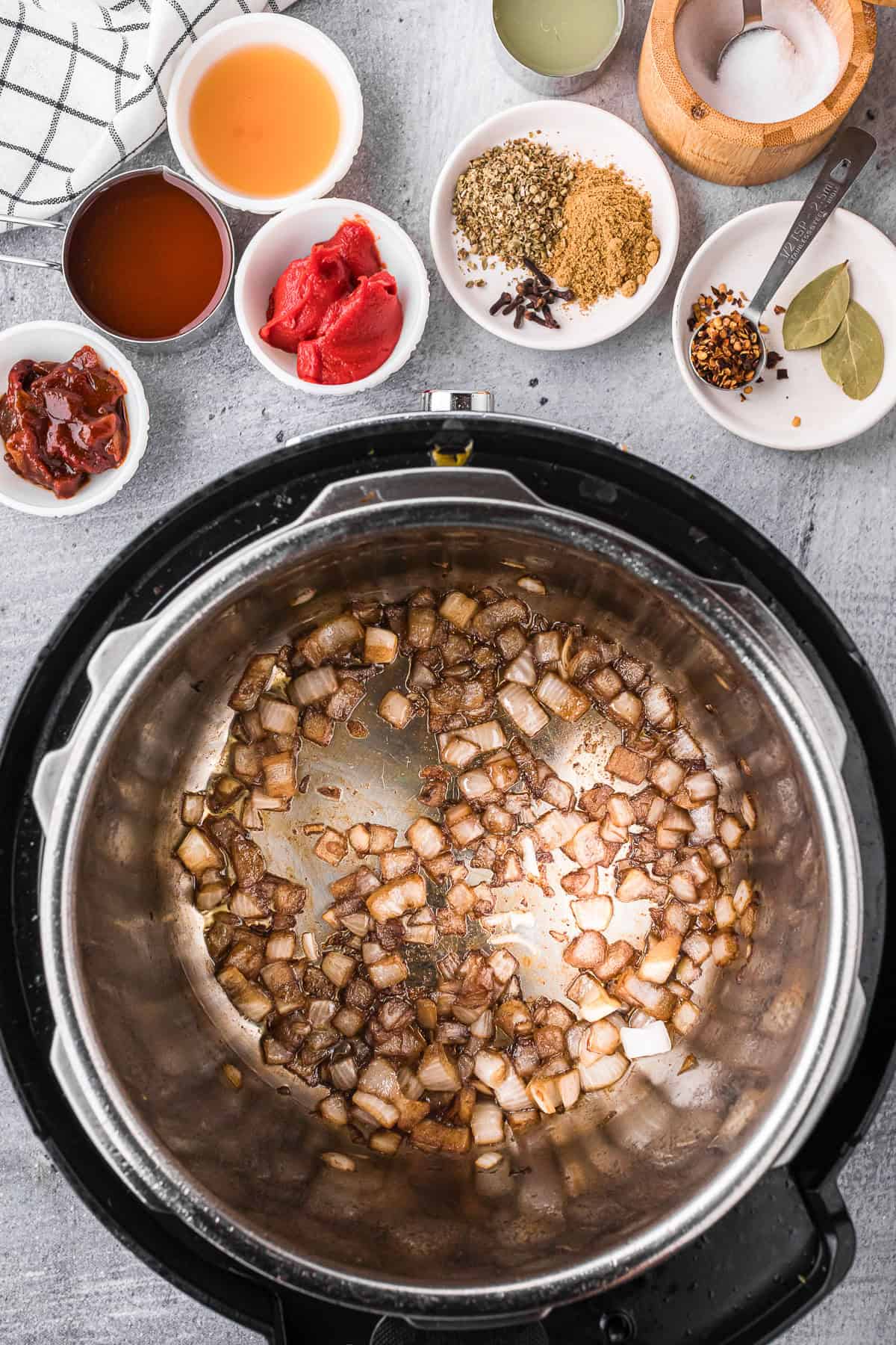 sauteing onions in an instant pot with small vessels of spices on the side.