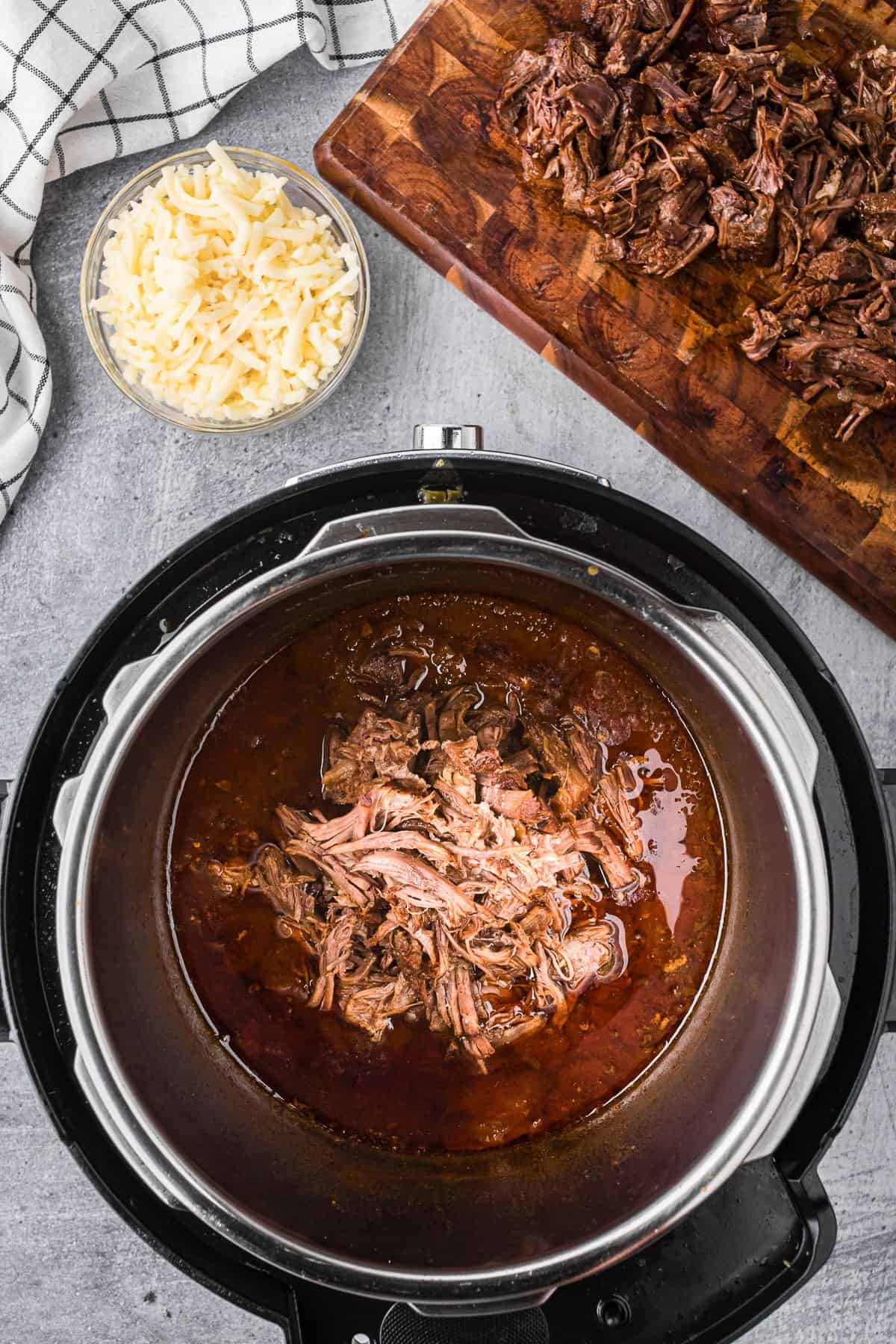 Adding shredded barbacoa beef back to cooking liquid in the instant pot.