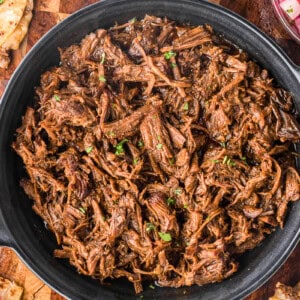 shredded barbacoa beef on black round dish with quesadilla triangles and pickled radish.