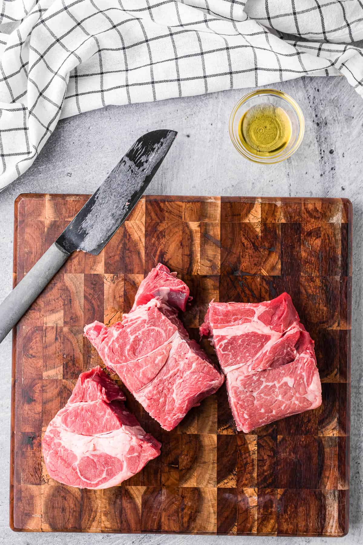 cutting a beef chuck roast into large chunks on a wooden cutting board.