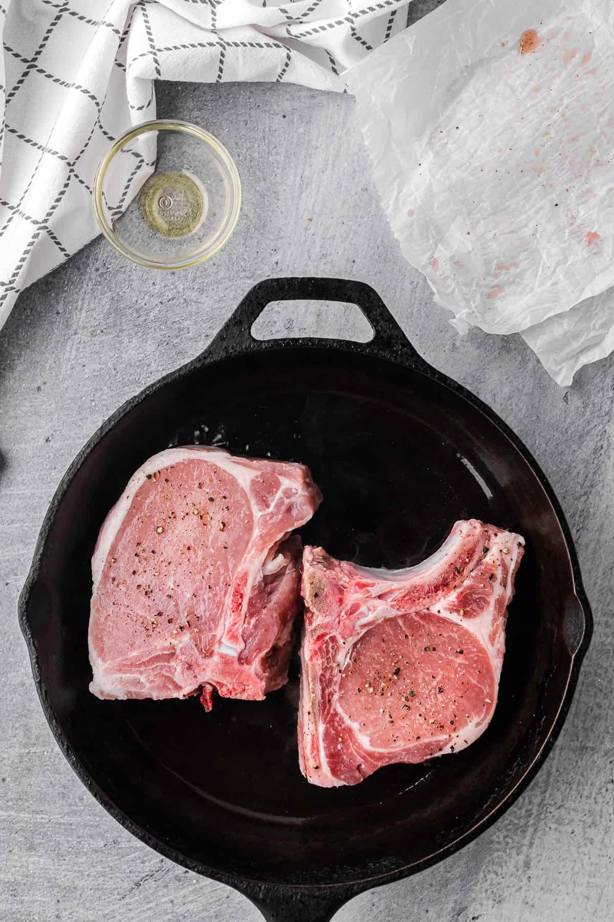 two bone in pork chops in a cast iron pan.