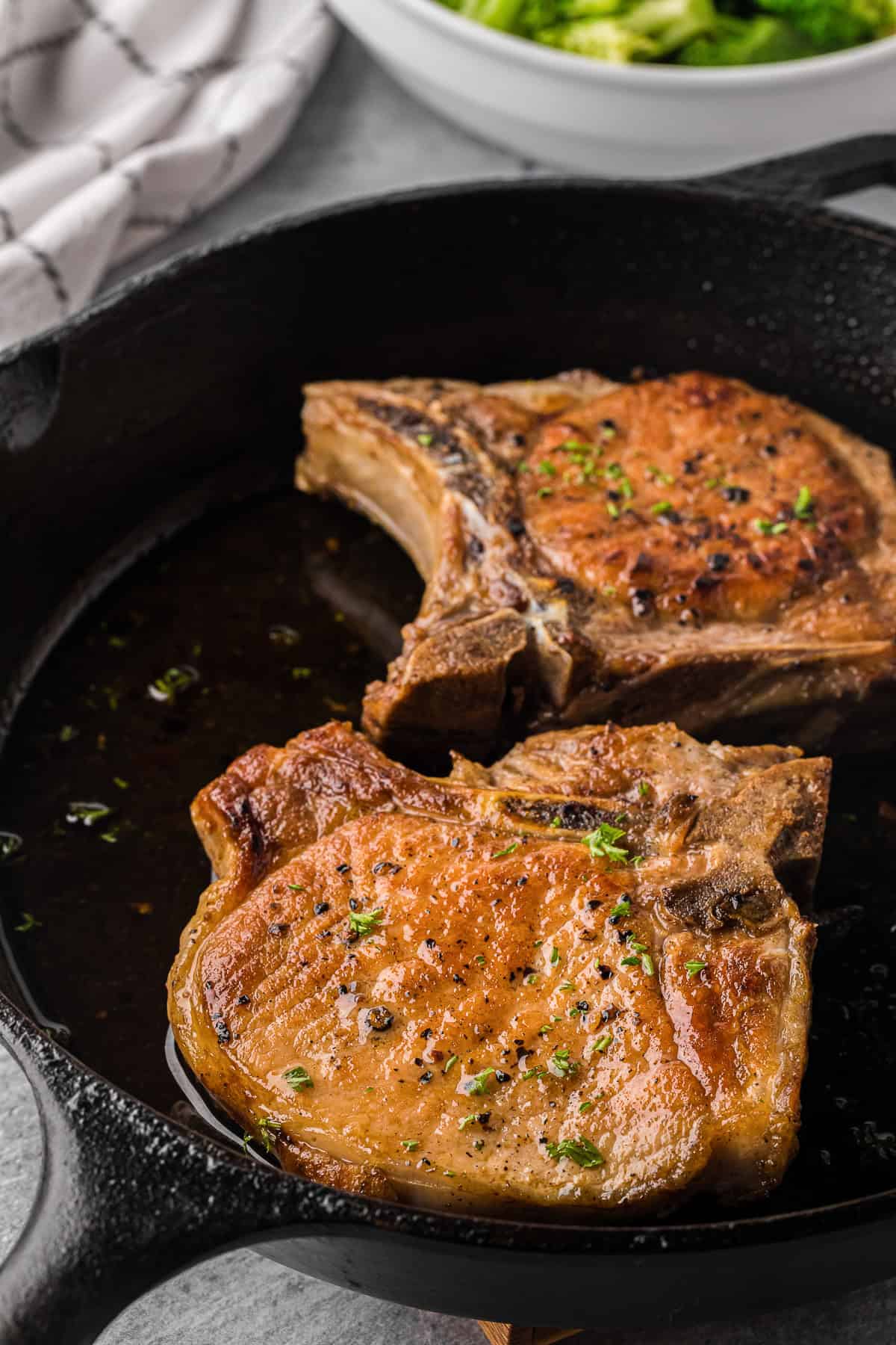 two pan seared pork chops in cast iron pan.