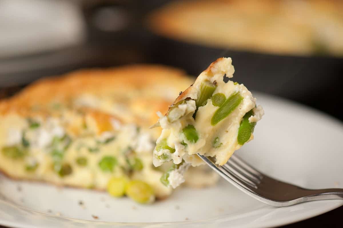 slice of spring vegetable frittata on plate with bite on fork.