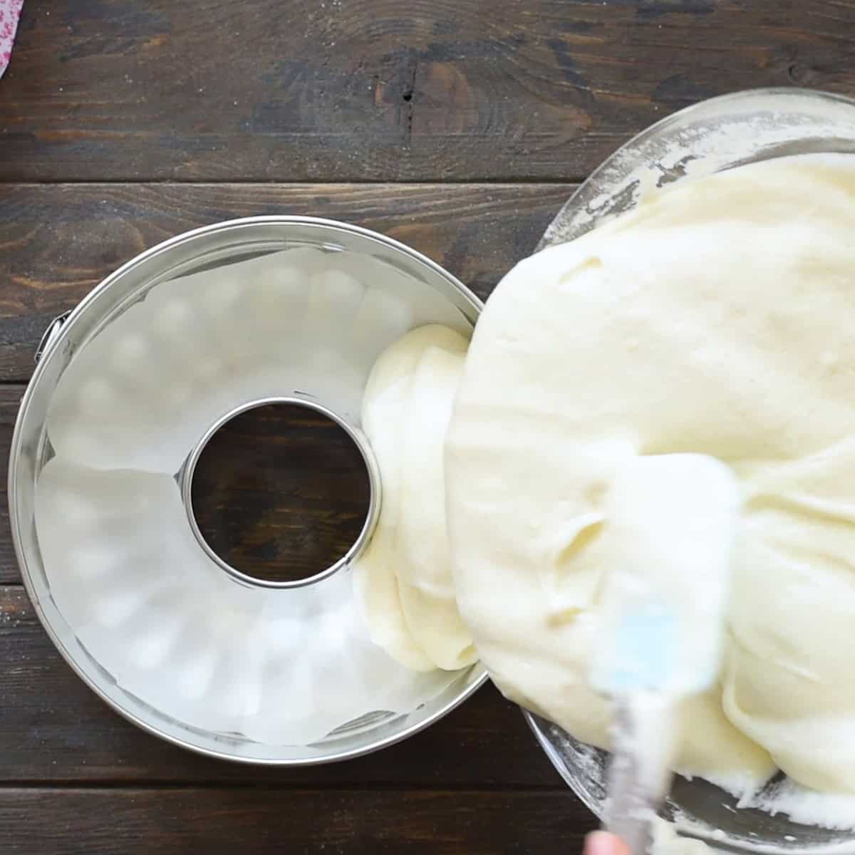 Pouring angel food cake batter into a prepared tube pan.