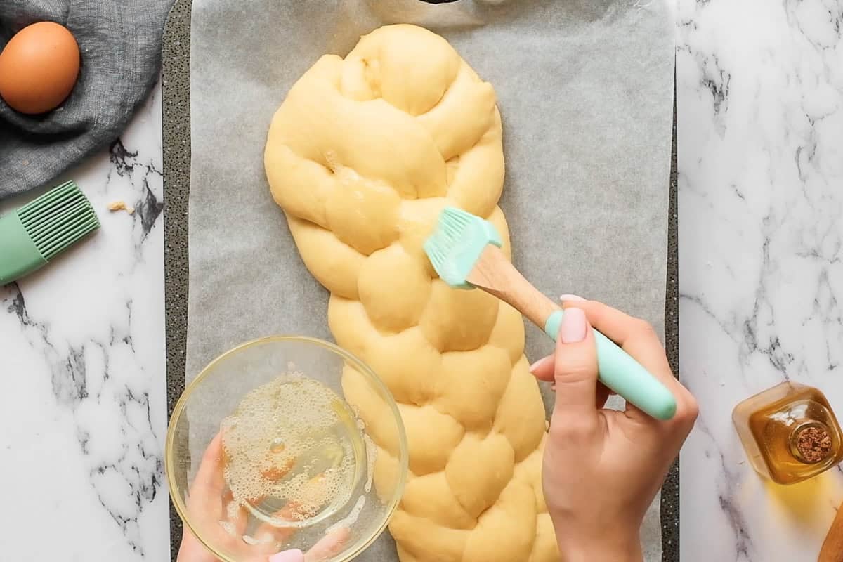 adding egg wash to homemade challah bread before baking.