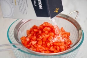 adding kosher salt to chopped roma tomatoes.