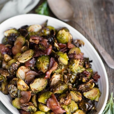 Air fryer Brussels sprouts with bacon in a white oval dish on a wooden table