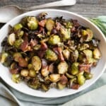 Brussels sprouts and bacon in a white oval serving dish with sage and rosemary