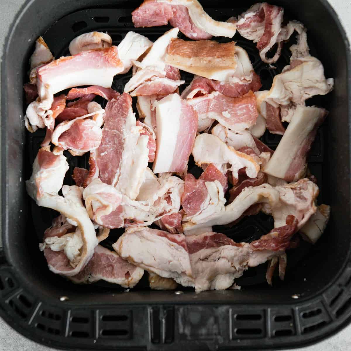 Raw bacon ends and pieces spread in an air fryer basket
