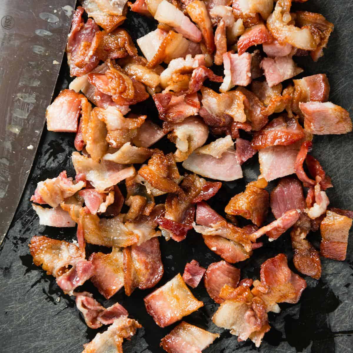 Partly cooked bacon chopped into bite-size pieces on a cutting board